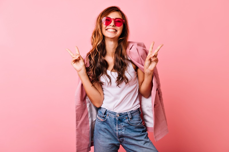 ragazza sorridente vestita con jeans, canotta e giacca e con occhiali da sole rosa