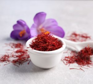 Coltivare zafferano; ciotola con stammi di zafferano essiccato; dietro fiori di zafferano,