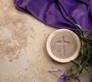 sfondo di pietra su cui sono posati mantello viola, palme, piatto di pietra con cenere in cui è stata fatta una croce; Mercoledì delle Ceneri