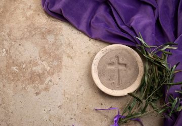 sfondo di pietra su cui sono posati mantello viola, palme, piatto di pietra con cenere in cui è stata fatta una croce; Mercoledì delle Ceneri
