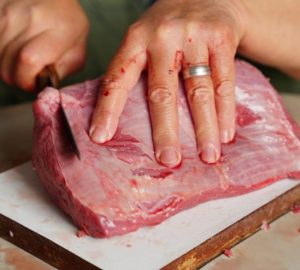 La carne di cavallo divide ancora tra tabù e regole diverse: Immagine dettagliata di mani che, con un coltello, tagliano un…