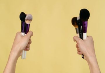Contouring per principianti: tecniche semplici per definire il viso: Due mani che tengono vari pennelli per trucco su uno…
